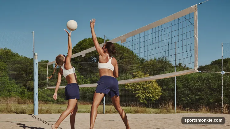 Two-player beach volleyball rally on a sand court with the ball above the net