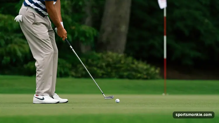 Golfer playing a low chip from the fringe, ball running toward the flag on the green