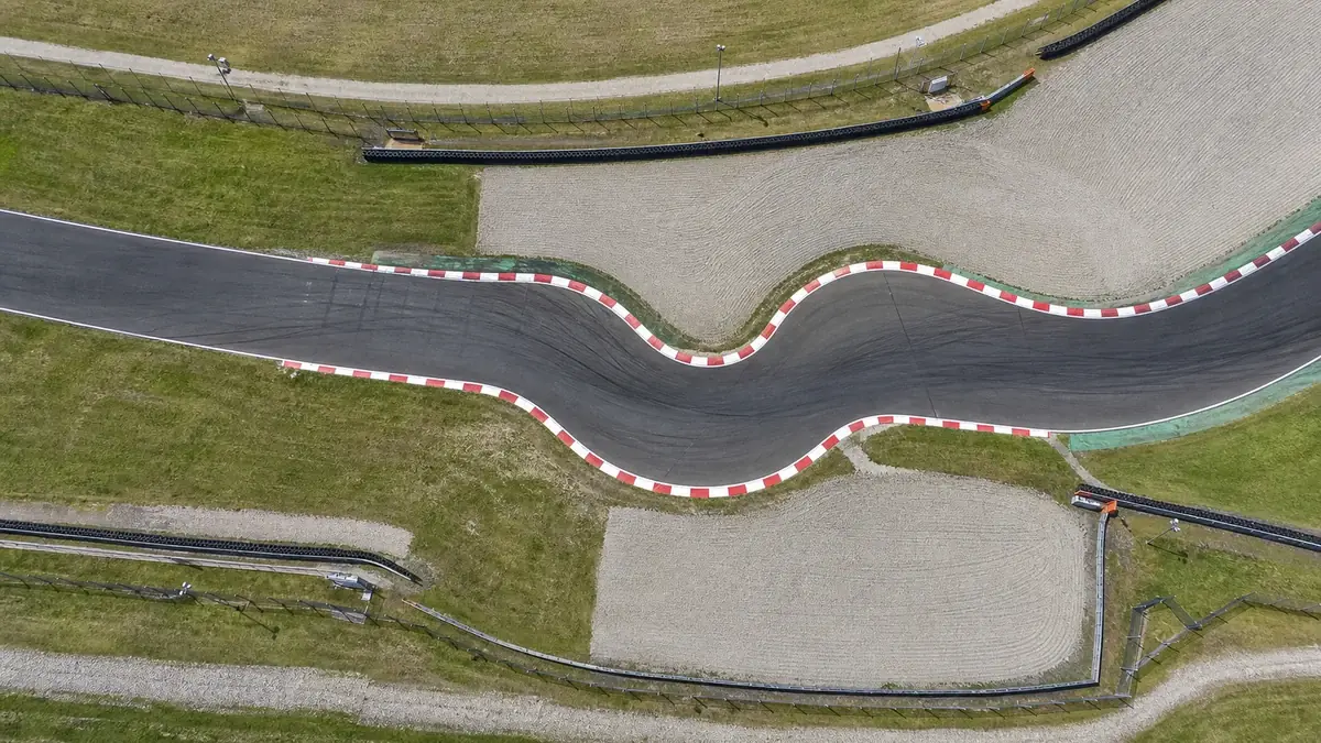 Overhead view of a tight S-shaped chicane section of a racetrack with red-and-white kerbs, empty track, no cars