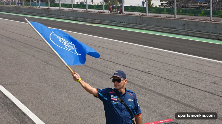 A marshal waving a blue flag at the side of a Formula 1 circuit as a car approaches