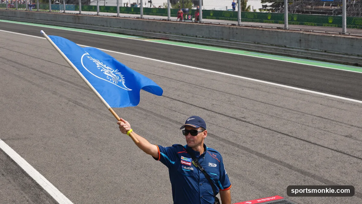 A marshal waving a blue flag at the side of a Formula 1 circuit as a car approaches