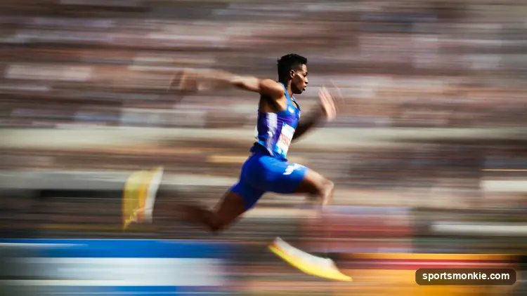 Male sprinter accelerating down an outdoor track in a packed stadium