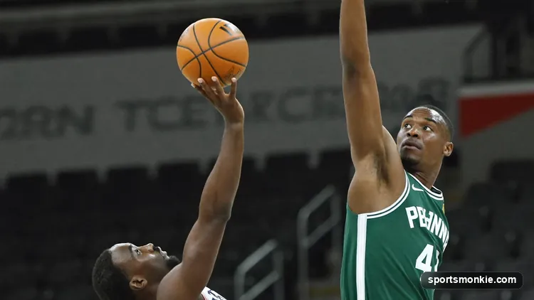 A basketball player releasing a finger roll shot off the fingertips near the rim