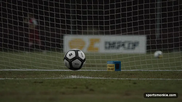 A soccer ball crossing the goal line into an empty net under floodlights