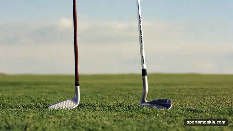 A golfer standing over a hybrid and a long iron laid side by side on the fairway, choosing a club