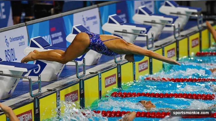 Four swimmers on starting blocks preparing for a medley relay exchange in a competition pool
