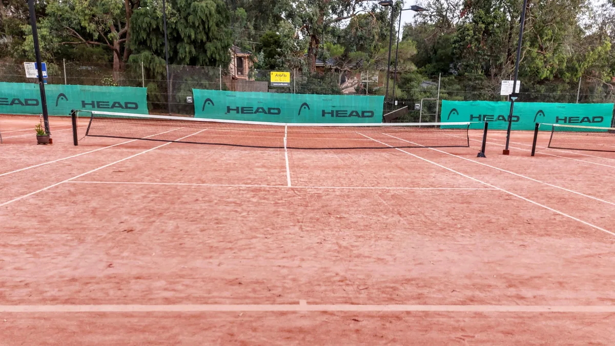 File photo from 21 January 2023: an empty clay tennis court in Melbourne, Australia, photographed looking down the net. It does not show Milicevic or any ITF event. The cropped 16:9 derivative is offered under the same CC BY-SA 4.0 licence as the original.