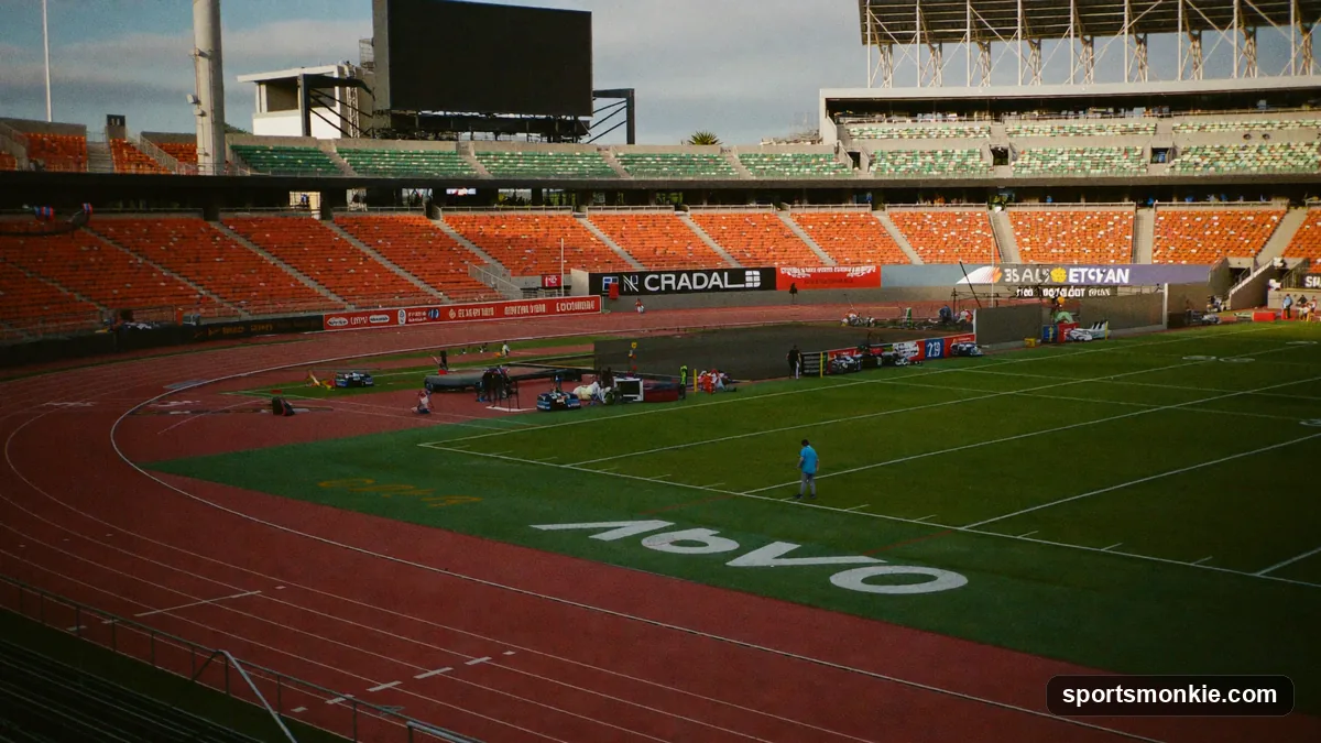 Wide shot of a track and field stadium showing the running oval, throwing sectors, and jump pits during competition