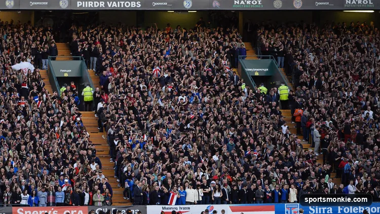 Two sets of rival football fans in contrasting colours filling a stadium on derby day