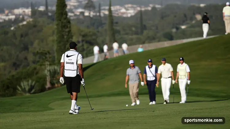 A caddie in a bib standing down the fairway watching a group of golfers tee off on a resort course