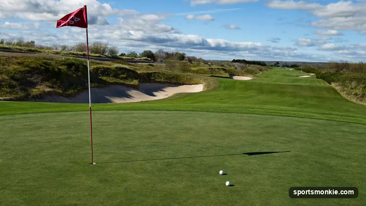 Golfer hitting an approach shot toward a distant green framed by bunkers on a sunny course