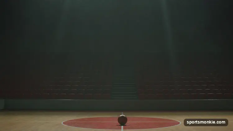 Empty basketball arena with a lit scoreboard and rows of vacant seats