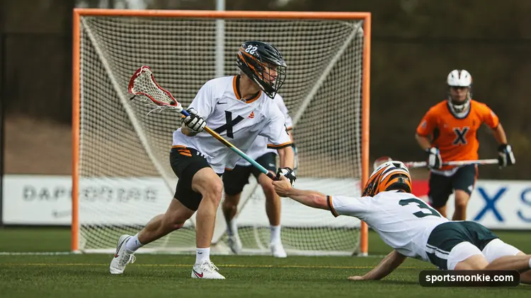 An attackman carrying the ball behind the goal looking to feed a cutting teammate during a lacrosse game
