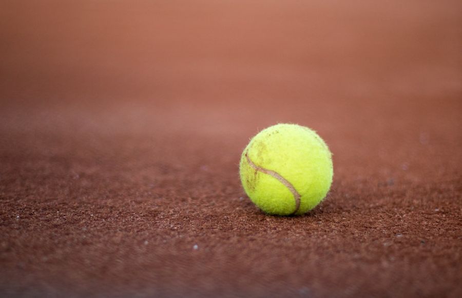 A yellow tennis ball in a clay court